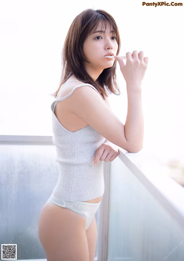 A woman in a white tank top and panties smoking a cigarette.