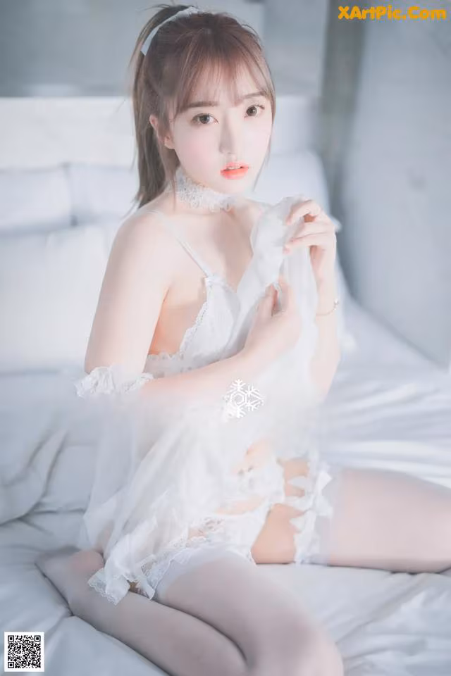 A woman in a white lingerie sitting on a bed.