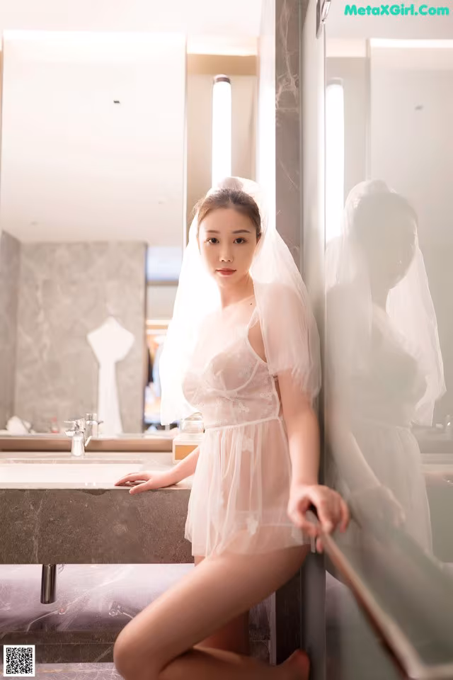 A woman in a white dress sitting on a bathroom counter.