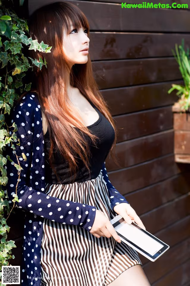 A woman leaning against a wall holding a tablet computer.