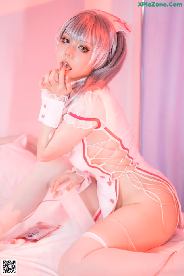 A woman in a pink and white outfit sitting on a bed.