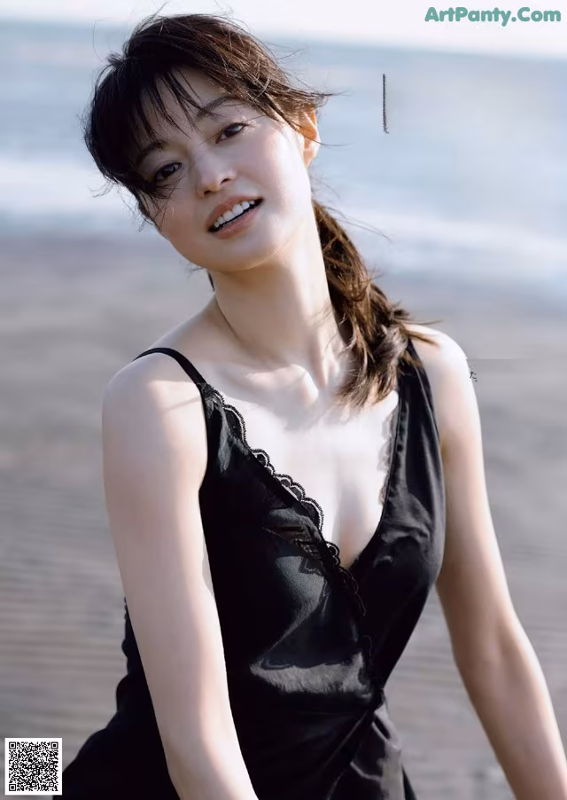A woman in a black dress posing on the beach.