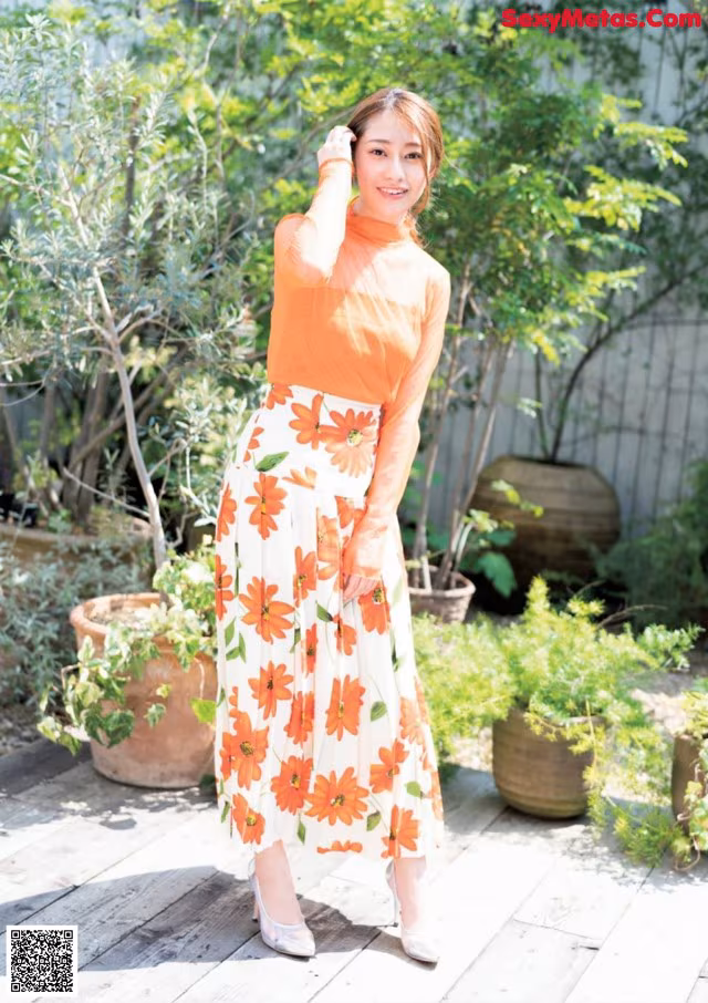 A woman in an orange top and a white skirt posing for a picture.
