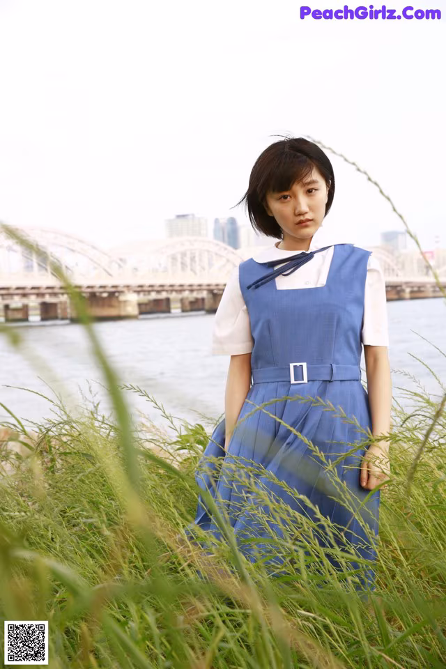 A woman in a blue dress standing in tall grass.