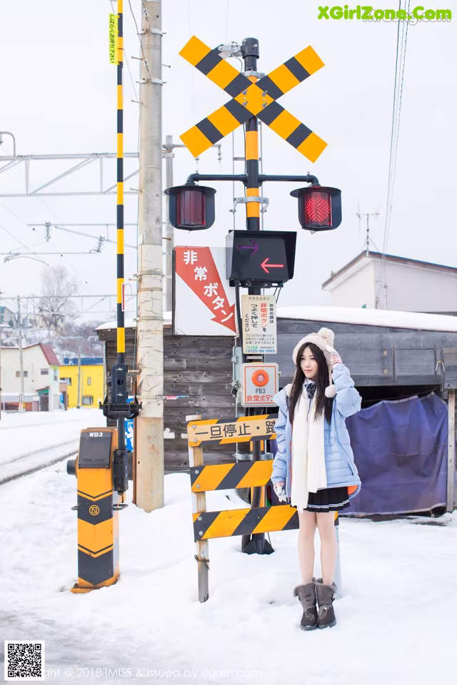A woman standing next to a railroad crossing in the snow.