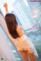 A woman in a white dress standing by a window.