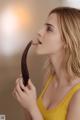 A woman in a yellow tank top eating a chocolate banana.