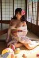 A woman in a kimono sitting on the floor with a flower in her hair.