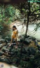 A woman in a yellow bikini standing on rocks by a river.